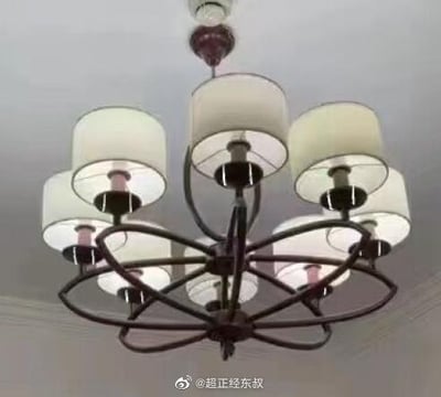 图片展示了一盏悬挂于室内天花板的吊灯，主体采用黑色金属支架，呈环形交错设计，共连接6个白色布艺灯罩，每个灯罩内装有灯泡，整体造型简约现代。图片底部中央可见微博用户水印“@超正经东叔”，无其他文字内容或人物出现。