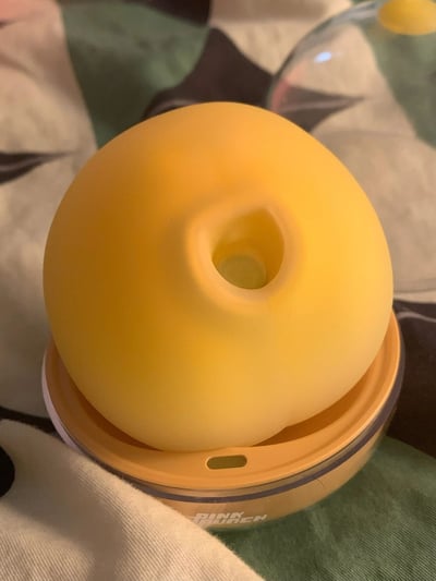 一张黄色圆形带孔玩具的照片，玩具表面光滑，中间有一个圆形孔洞，放置在一个橙色盖子的透明容器上。背景是带有花纹的布料。