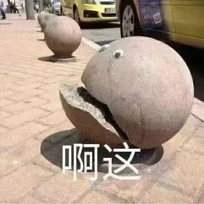 图片展示了人行道上的一排圆形石墩，其中前景的石墩因表面开裂形成了类似“嘴巴”的形状，被网友添加了两只黑色圆点作为“眼睛”，整体呈现出一副惊讶或错愕的表情。石墩下方配有白色文字“啊这”，这一网络热词常用来表达意外、尴尬或不知如何回应的情绪。背景中可见街道、黄色车辆和行人，营造出真实的街头场景。图片通过对日常物体的趣味改造，形成了幽默的视觉效果。
