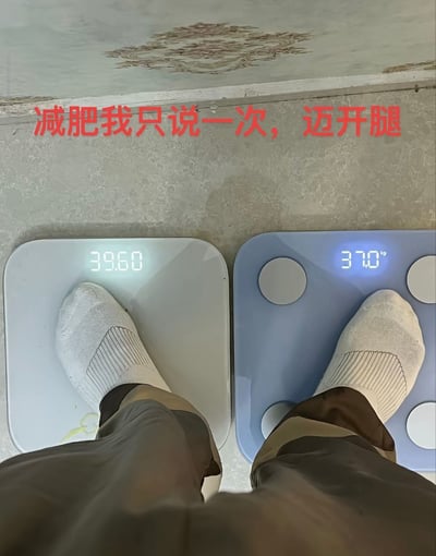 图片为俯视视角，展示一个人双脚分别踩在两个体重秤上：左侧秤显示39.60kg，右侧秤显示37.0kg。上方有红色醒目文字“减肥我只说一次，迈开腿”。通过左右脚踩不同秤的体重差异，幽默演绎“迈开腿”这一减肥口号——字面意义上“迈开腿”到另一个秤，体重立刻变轻，形成搞笑反差。