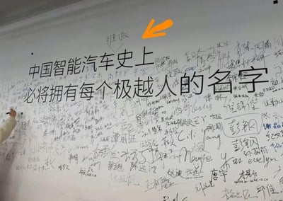 这是一面极越汽车的员工签名墙，墙面上印着醒目的大字“中国智能汽车史上必将拥有每个极越人的名字”，整面墙被密密麻麻的员工手写签名覆盖，画面左侧可见一只手正在墙上签名，满墙的签名承载着员工对企业的认同与对品牌在智能汽车领域发展的信心，整体氛围充满团队归属感与使命感，图中没有双关、谐音梗或暗示内容。