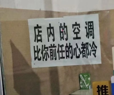 这是一张拍摄线下店铺玻璃门的照片，玻璃上贴着一张白色纸质标语，用醒目的黑色字体写着“店内的空调比你前任的心都冷”，以网络上常见的调侃前任的搞笑梗来夸张地宣传店内空调的制冷效果，风格幽默接地气，容易引发顾客的共鸣和兴趣。玻璃右下角可见“推”字标识和一个绿色小包装物品，标语纸张上还覆盖有“沙雕群546370479”的社群水印。