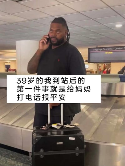 这张图片拍摄于机场行李提取区域，画面中一位身材壮硕的黑人男性站在行李传送带旁，一手将手机贴在耳边打电话，一手扶着行李箱拉杆，他的眼神带着软萌的依赖感，和自身壮硕的身材形成强烈反差。图片上叠加了白色背景的中文文字：“39岁的我到站后的第一件事就是给妈妈打电话报平安”，用这种反差感的画面，传递出无论年龄多大，在母亲面前依然是需要报平安的孩子的温情内核，能够引发人们对亲情的共鸣。
