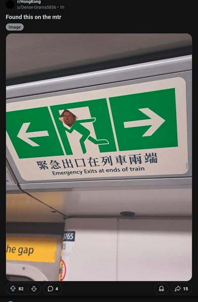 这是一张在香港地铁车厢内拍摄的照片，照片中原本标准的绿色紧急出口标志被人恶搞，标志上奔跑的白色人形图案头部被替换成一张表情夸张的男性面孔，显得十分滑稽有趣。标志下方有中英文文字"緊急出口在列車兩端 / Emergency Exits at ends of train"。照片下方还能看到部分黄色的"Mind the gap"警示标识。