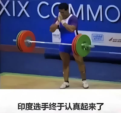 图片中是一位身着蓝紫色运动服的举重运动员，正双手合十置于胸前，身后是一根装有红色和绿色杠铃片的杠铃。背景为蓝色，上面有部分白色文字“XIX COMMO”。图片底部配有文字“印度选手终于认真起来了”，整体营造出一种期待运动员认真比赛的幽默氛围。