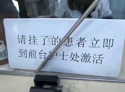 这是一张实拍的医院窗口静态图，玻璃内侧摆放着一张白色的打印告示，原本的内容是提示挂号后的患者到护士处激活，但是“号”字被人用手写的数字3覆盖修改，使得句子容易被误读为“请挂了的患者立即到前台护士处激活”，中文里“挂了”有去世的含义，和“激活”形成了荒诞的反差，产生了搞笑的喜剧效果，告示前方有窗口传声用的麦克风穿过，背景能模糊看到穿白大褂的医护人员身影。