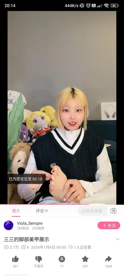 这是一张哔哩哔哩（B站）的竖屏视频截图，画面中浅金色头发的视频作者Viola_Sempre正微笑着展示自己的脚部美甲，脚趾甲做了多种风格的美甲设计，包括红色纯色、带图案的款式，她的双手扶着脚。背景中可以看到多个毛绒玩偶，视频界面显示该视频标题为《三三的脚部美甲展示》，发布于2024年1月6日，播放量2.7万，当前有1人正在观看，作者拥有280粉丝，已发布295个视频。画面中还有“已为您定位至02:10”的定位提示文本。整体风格轻松日常，是作者分享自己美甲的原创视频内容。