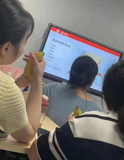 图片中三位女性正聚精会神地观看屏幕上的教学内容，屏幕上显示的是"男性增硬手法6式"的教学PPT，包括霸王鞭、月下飞、组合拳等招式。巧合的是，三位女性手中都拿着香蕉，与屏幕上的敏感内容形成了滑稽的呼应，营造出一种尴尬又搞笑的氛围。