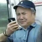 一位戴着蓝色帽子的中年男性，身穿蓝色衬衫，正单手举着手机查看，眉头微皱，嘴角下撇，表情中透露出明显的无奈与困惑，仿佛在手机上看到了什么令人不解的内容。背景模糊，无法清晰辨认具体环境，但整体给人一种日常生活中遇到小烦恼的感觉。