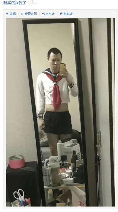 这是一张社交媒体帖子截图，帖子标题标注“新买的jk到了”。画面主体是一位寸头男生在室内全身镜前自拍，他穿着短款白色JK水手服上衣，搭配标志性的红色领结，上衣长度较短，露出了腹部，下装则是一条普通的黑色短裤，整体穿搭和大众认知中JK制服的甜美女生风格形成强烈反差，制造出搞笑、滑稽的趣味效果。画面下方是室内的桌面区域，摆放着水壶、各类瓶罐杂物，旁边的黑色柜子上放着粉色胶带，柜子前的容器里还有剪刀等文具，呈现出日常居家的场景。