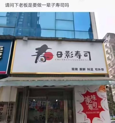 图片展示了一家名为“春日影寿司”的日式料理店临街店面，白色招牌上印有黑色飞鸟图案、红色圆形元素及寿司简笔画，下方标注“现做 新鲜 料足 可外带”。图片顶部叠加文字“请问下老板是要做一辈子寿司吗”，通过将店名与“一辈子”的幽默关联，形成轻松搞笑的吐槽效果。背景可见现代玻璃幕墙建筑，整体场景为真实街拍环境。