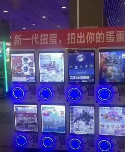 图片展示了一排扭蛋机，上方有一个红色横幅，上面写着“新一代扭蛋，扭出你的蛋蛋”。扭蛋机共有两层，每层四个，每个机器都有蓝色的圆形按钮和展示窗口，窗口里显示着不同的扭蛋内容图片。整个场景灯光偏紫色，看起来像是在商场或游戏厅等娱乐场所。

标语中的“蛋蛋”存在双关含义，字面意思是指扭蛋机里的蛋形玩具，但在中文口语中“蛋蛋”也是对男性睾丸的戏称，这种意外的谐音梗让普通的商业标语产生了搞笑效果。