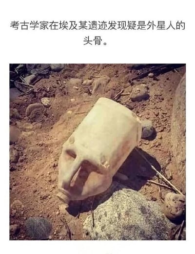 这是一张图文混排的搞笑趣味图片，上方配有文字“考古学家在埃及某遗迹发现疑是外星人的头骨。”，下方的实拍图展示了一个被遗弃在泥土与石块中的旧塑料水壶，该水壶的提手区域因造型和表面污渍，恰好形成类似人脸眼眶与鼻子的视觉效果，被刻意和上方的文字结合，营造出“发现外星人头骨”的乌龙假象，利用视觉错觉制造反差笑点，调侃了一些夸张的考古传闻类内容，整体风格诙谐幽默。