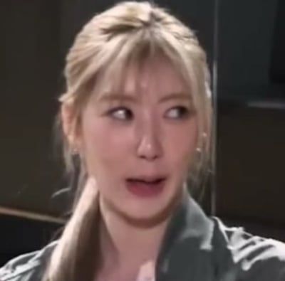 这张图片展现了一位金发长发的女性，穿着较为休闲，似乎正在与人对话。从发型和服装来看，整个画面给人一种轻松的生活化氛围。背景较暗，可能是室内拍摄，如访谈、综艺或电视剧片段。