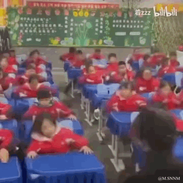 这是一段记录教室日常的动态GIF，画面中一群穿着统一红色校服的小学生坐在蓝色课桌前，随着画面推进，学生们陆续趴在课桌上，动作整齐又带着困倦感，真实还原了学生上课犯困时的状态，场面搞笑又贴近校园生活。图中没有双关、谐音梗或暗示内容。