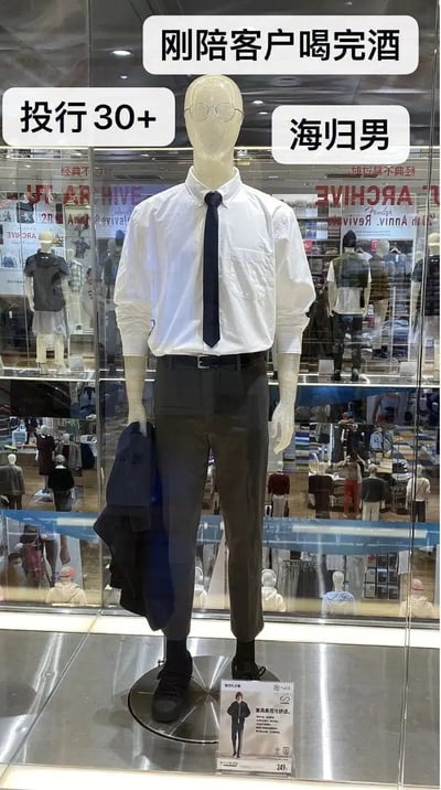 这是一张服装店橱窗里的男士模特照片，模特身穿白衬衫、领带和较为正式的裤装，脚踏皮鞋，左手挂着一件西装外套。图片通过PS或贴纸，在模特头部和身体两侧分别加了“海归男”“投行30+”“刚陪客户喝完酒”几个标签，搞笑地模仿了都市精英男士的日常形象。整体充满了对海归、投行男、30+职场男性生活的调侃，具有一定的自嘲与讽刺意味，将精英职场与现实压力幽默结合。

存在明显的都市职场男性双关调侃和对“人间打工人”形象的戏谑。