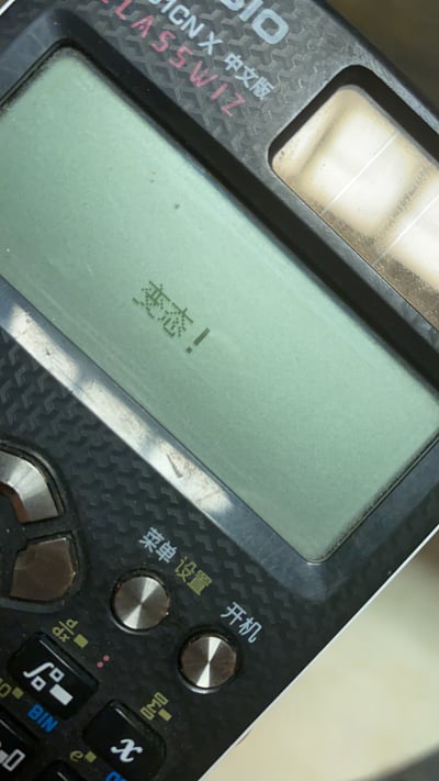 这是一张卡西欧（CASIO）CN X 中文版计算器的实拍图，计算器屏幕上显示着中文“变态！”，显然是用户通过计算器的文字输入功能自定义显示内容，用来表达吐槽、不满的情绪。计算器外观带有使用痕迹，按键区域的“菜单 设置 开机”等标识清晰可见，整体是日常用电子设备作为情绪表达载体的场景，没有双关、谐音梗等特殊设计，只是直白的情绪输出。