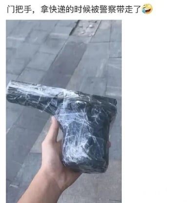 图片中一只手握着一个被塑料膜包裹的黑色门把手，放置在石质地面上。上方配文'门把手，拿快递的时候被警察带走了😂'，暗示因门把手外形可能被误认为可疑物品，导致拿快递时被警察带走的搞笑误会场景。