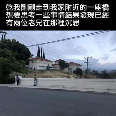 图片上方为文字描述：“乾我刚刚走到我家附近的一座桥想要思考一些事情结果发现已经有两位老兄在那里沉思”。下方是一张实拍照片，展示了一条街道的场景，道路旁有一堵白色的长墙，墙前站着两位背对镜头的人，似乎在低头沉思。背景中可以看到几栋带有红色屋顶的住宅建筑，周围有茂密的树木和高耸的柏树，天空中布满云层，整体氛围较为宁静。