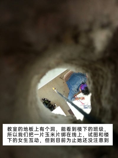 这张图片以教室地板上的破洞为拍摄视角，向下拍摄楼下的班级。画面中可见楼下班级里一位穿着牛仔外套、头发带有紫色挑染的女生正低头专注于手头的事务，楼上的人将一片玉米片绑在线上，从地板的洞里垂下去，试图用这个有趣的小把戏和楼下的女生互动，不过从画面来看，女生目前还没有注意到这个来自上方的“趣味邀请”。图片下方配有文字说明，解释了这个场景的来龙去脉，整体充满了学生时代调皮搞怪的轻松氛围，是校园生活里的即兴趣味整活。