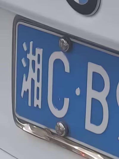 这是一张近距离拍摄的中国大陆民用汽车牌照特写，蓝底白字的牌照开头为“湘C·B”，其中“湘”是湖南省的简称，“湘C”代表该车辆归属地为湘潭市。牌照配有金属边框，画面上方能看到宝马（BMW）车标的一角，拍摄视角聚焦在牌照左侧区域，清晰呈现了牌照字体、固定螺丝等细节，整体画面为实景拍摄，无二次创作或谐音梗等特殊内容。