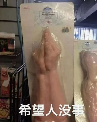 图片展示了一个包装好的祈祷手势玩具，商品名称为'Mr. Double Five Baby Talker or Handman'，价格为9.99美元。玩具造型为双手合十祈祷的姿势，被透明塑料固定在纸板包装上。图片底部有中文文字'希望人没事'，暗示这个产品造型可能略显怪异或令人担忧。背景显示这是在商店环境中拍摄的，能看到其他商品货架。