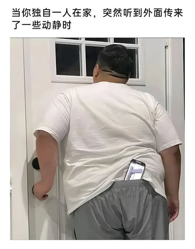 图片展示了一个独自在家的人听到外面有动静时的反应：一名穿着白色T恤和灰色裤子的男子正小心翼翼地通过门上的窗户向外查看，同时他的手机从后口袋露出，摄像头已打开对准门外方向，似乎在不直接开门的情况下记录外面的情况。这种既想知道外面发生了什么又保持警惕的矛盾心理，生动展现了独居时面对突发状况的真实反应。