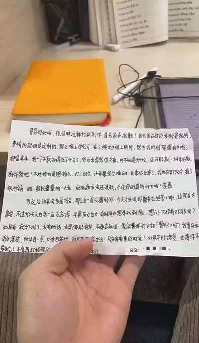 图片中一只手正拿着一张手写信件，背景是摆放着黄色笔记本、书籍、耳机和电子设备的书桌，呈现出典型的学生学习环境。信件内容为一名考研寄宿女生的自述：她在6楼卫生间听到隔壁男生隔间的声响后产生兴奋感，因对方“持久”而感到“难耐”，随后在洗手时瞥见对方内裤“鼓鼓囊囊”，推测“还没设”并表示“羡慕”。信中还提到偶然发现对方在经管1班，以“压力大想找刺激”为由，询问对方是否有女友，若没有则请求成为能“帮忙打飞机、口”的性伴侣，并留下QQ号（已打码）。信件语言直白露骨，内容涉及隐私窥探与不当性暗示，整体氛围尴尬且令人不适。
