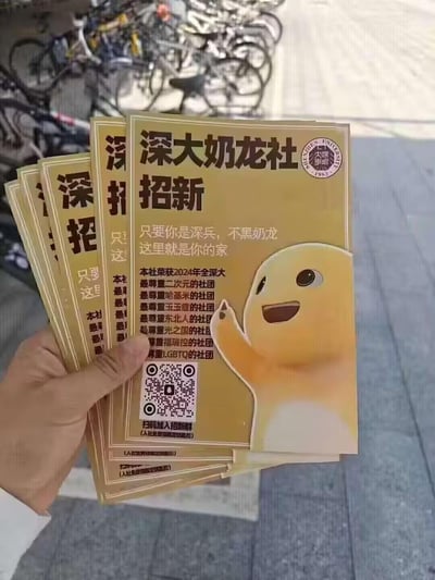 这是一只手拿着几张深圳大学奶龙社的招新传单，传单以暖黄色为底色，印有卡通角色奶龙的开心挥手形象。招新标语为「只要你是深兵，不黑奶龙，这里就是你的家」，还列出了一堆搞笑的「荣誉称号」，包括最尊重二次元、哈基米、玉玉症、东北人、光之国、福瑞控、LGBTQ的社团，用玩梗的接地气风格吸引同好加入，下方附有扫码入群的二维码，还标注入社可领限定钥匙扣，右上角有深圳大学1983的校徽样式标识，整体风格幽默亲切，充满校园趣味。