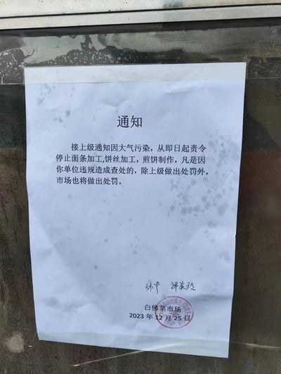 这是一张拍摄于玻璃表面的纸质通知照片，通知由白佛菜市场于2023年12月25日发布。内容显示，因大气污染防控要求，接上级通知从即日起责令市场内商户停止面条加工、饼丝加工、煎饼制作；若商户违规被查处，除上级部门处罚外，市场也将另行处罚。通知纸张表面有污渍，底部有签名、市场名称及红色公章。