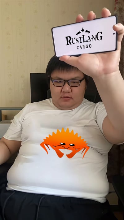 这是一张趣味错位合成梗图：一位戴眼镜的胖男士坐在椅子上，他的腹部被合成了Rust编程语言的吉祥物Ferris螃蟹，同时男士举着显示“RUSTLANG CARGO”的手机放在头顶，通过视觉错位让手机看起来像是给肚子上的螃蟹“戴上了帽子”。玩了Cargo（Rust的包管理工具）和“肚（腹）蟹”的谐音错位梗，用搞笑的形式调侃Rust开发者与工具的关联，画面充满趣味。