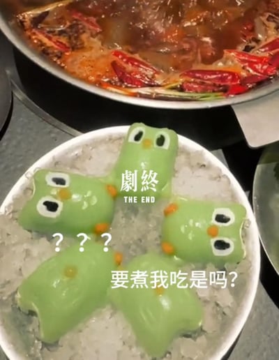 图片展示了一个有趣的美食场景。前景中有一个装有冰块的白色盘子，上面放着四个绿色青蛙形状的食物，它们有着黑色的大眼睛和橙色的腮红。背景是一个正在沸腾的火锅，里面有红色的辣椒和各种食材。青蛙形状的食物似乎正面对着火锅，图片上的文字"要煮我吃是吗?"赋予了它们拟人化的担忧情绪，仿佛在担心自己会被放进火锅里煮。上方还有"劇終 THE END"的文字，增加了幽默感。