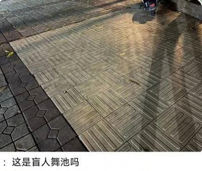 这是一张趣味玩梗的实拍图，图中展示了一处户外铺砖地面，一整片大面积区域都铺满了带有同向平行凹槽纹路的盲道砖，砖面潮湿带有反光，仅在图片左侧拼接了深灰色异形步道砖，图片底部配有调侃文字“这是盲人舞池吗”，借大面积同向纹路盲道的外形相似性调侃，将其戏称为盲人舞池，属于搞笑玩梗内容。
