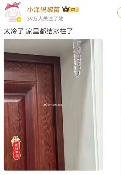 这是微博用户“小泽犽黎苗”发布的一条动态，配文“太冷了 家里都结冰柱了”，并附上一张实拍图。图中展示了自家门框上方墙角处悬挂的一根透明冰柱，门上还贴着写有“有住有闹”的红色装饰，用真实的结冰场景直观体现室内温度极低的状况，以此调侃寒冷的天气，容易引发网友对低温生活的共鸣。