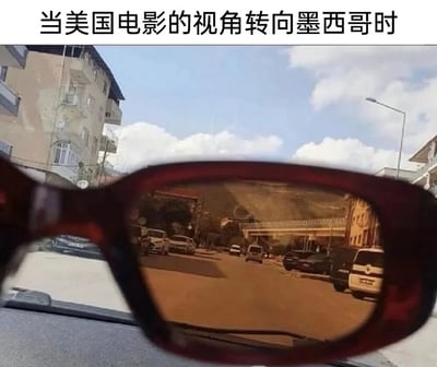 图片展示了一副太阳镜，镜片反射出的景象呈现出典型的美国电影中对墨西哥的刻板印象——沙漠、土路和简陋建筑，而实际透过镜片看到的则是现代化的城市街道。这种反差幽默地讽刺了美国电影对墨西哥的片面描绘。