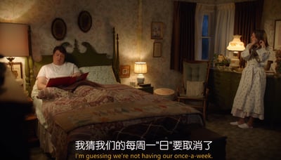 这是一个夜晚的复古风格卧室场景，房间布置温馨，带有老式花纹壁纸和复古家具。床上的男性穿着白色T恤，正靠在床头阅读红色封面的读物，表情平淡；画面右侧的女性穿着碎花睡袍，站在梳妆台前，双手放在耳边，神情带着失落。画面底部配有中文字幕“我猜我们的每周一"日"要取消了”，对应的英文是“I'm guessing we're not having our once-a-week.”，其中“日”是谐音梗，指代夫妻间约定的每周亲密互动，暗示这次的计划将要泡汤，整体氛围带着无奈与小失落。