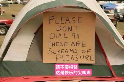 这是一张户外露营场景的实拍照片，画面中心是一个绿白红三色拼接的露营帐篷，帐篷入口处立着一块手写的硬纸板提示牌，上面用黑色字体写着英文提示语，图片下方配有粉色底的简体中文翻译“请不要报警 这是快乐的尖叫声”。背景可见户外的草地、红色的车辆以及远处其他的露营房车和帐篷，整体场景是典型的露营营地环境。这块提示牌是帐篷内的露营者为了避免外界将他们发出的快乐尖叫误会成求救声而报警特意设置的，充满了搞笑趣味。
