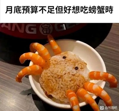 这张图片呈现了一个充满生活趣味的创意美食：当月底预算不足却想吃螃蟹时，网友用米饭团成螃蟹身体的形状，淋上酱汁模拟蟹壳的色泽与质感，用两颗深色小颗粒作为螃蟹的眼睛，再将虾尾摆放成螃蟹的八条腿，放置在白色小碗中，逼真地模仿出螃蟹的形态。图片上方配文“月底预算不足但好想吃螃蟹时”，精准戳中了月底拮据却嘴馋的状态，用低成本的食材组合出想吃的美食造型，既搞笑又充满巧思。