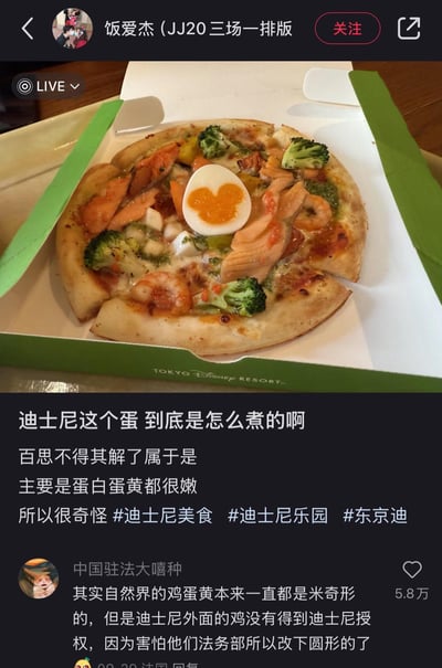 这是一张抖音直播的截图，展示了东京迪士尼度假区的一款特色海鲜蔬菜披萨，最引人注目的是披萨上的溏心蛋，蛋黄被塑造成了米奇头的形状。发布者发文疑惑这个蛋的制作方法，称蛋白和蛋黄都很嫩，对此百思不得其解。下方热门评论玩起了迪士尼法务部的梗，调侃说自然界的鸡蛋黄原本都是米奇形状，外面的鸡因为没得到迪士尼授权，害怕法务部才改成圆形，十分搞笑。