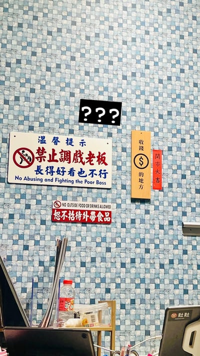 # 温馨搞笑禁止调戏老板的提示墙

图片展示了办公室或小店墙面贴满幽默提示牌，最显眼处是一块写有“禁止调戏老板，长得好看也不行”的警示牌，用中英双语表达，语气调侃却有趣。其中“老板长得好看也不能调戏”，明显带有自嘲与自夸意味，整体气氛轻松幽默。旁边还有“收钱的地方”、“问事大吉”等复古木牌，以及禁止自带外食的警告。最上方黑底白字的“？？？”更增添困惑感。

## 双关与暗示
- “长得好看也不行”属自夸式幽默，略带自恋、反差梗。
- “调戏老板”本为禁令，却用娱乐化表达，演化为员工/顾客间的社交梗。
- 整体有明显恶搞、无伤大雅的办公室或小店幽默气息。
