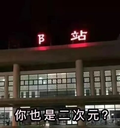 深夜场景下，一栋现代风格建筑的顶部被P上了红色发光的“B站”字样，建筑主体为多层结构，底层有大面积玻璃窗和白色立柱，内部透出灯光。图片底部叠加白色文字“你也是二次元？”，以调侃的语气将建筑与B站的二次元文化属性关联，营造出“这栋楼也是B站据点”的幽默效果，引发二次元爱好者共鸣。