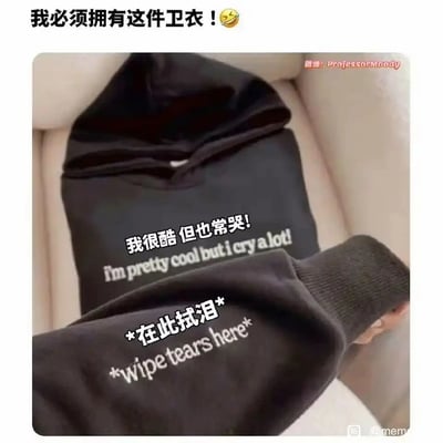 这是一张展示创意黑色连帽卫衣的静态图，卫衣的设计充满趣味与情绪共鸣：正面印有中文“我很酷 但也常哭！”和对应的英文“I'm pretty cool but i cry a lot!”，精准契合了不少人外表装作坚强、实则内心柔软爱哭的状态；卫衣的袖子区域还印有中文“*在此拭泪*”和英文“*wipe tears here*”，将袖子设计成专属的拭泪区域，让这件卫衣兼具实用性与情绪表达功能。图片顶部配文“我必须拥有这件卫衣！😆”，传递出网友对这件创意服饰的强烈喜爱，这类设计让服饰不再只是穿搭单品，更是一种情绪的出口与表达。