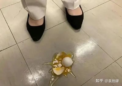 这是一张以俯视角度拍摄的照片：一个人穿着黑色平底鞋和白色裤子，站在光滑的地板上，前方地上有一个摔碎的鸡蛋。鸡蛋摔裂，蛋液和蛋壳散落一地，画面充满了“突发小意外”的无奈。它常被用来表达“事情突然搞砸”、“心情崩溃”或“今天的自己很倒霉”。

没有明显双关、谐音梗或暗示内容。