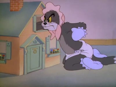 这是一张经典动画《猫和老鼠》的截图，画面中的汤姆猫身着一套婴儿风格的服饰，包括粉色婴儿帽、白色围兜以及浅蓝色的手套和脚套。它眉头紧皱，眼神凶狠锐利，嘴巴紧绷，满脸愤怒不满的神情，蹲在地面上，姿态看起来带着强烈的情绪。背景是一座带有小窗户、门和烟囱的迷你小房子，整体画面延续了《猫和老鼠》一贯的卡通诙谐风格，汤姆的愤怒表情与婴儿服饰形成反差，增添了滑稽感。