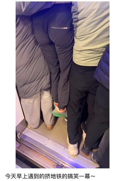 这是一张拍摄于城市早高峰地铁的实拍照片，画面中多名乘客拥挤在地铁车门区域，由于视觉错位效果，中间穿着深色带拉链运动裤的乘客的下半身，看起来像是“悬浮”在前方穿灰色棉服、浅灰牛仔裤乘客的腰侧位置，他的绿红配色运动鞋也仿佛和前方乘客的身体连在一起，制造出一种这名乘客被挤得“双脚离地”的滑稽错觉。图片下方配文“今天早上遇到的挤地铁的搞笑一幕～”，点明了这是早高峰通勤时遇到的趣味场景，既真实展现了城市早高峰地铁拥挤的现状，又因这个巧合的视觉错位让原本疲惫的通勤场景变得充满笑点。