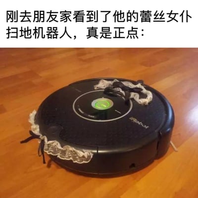 图片展示了一台黑色的iRobot扫地机器人，其侧面被装饰了白色蕾丝花边和黑色蝴蝶结。扫地机器人放置在木质地板上，顶部有绿色指示灯亮起。图片上方配有文字："刚去朋友家看到了他的蕾丝女仆扫地机器人，真是正点："。

该图片使用了双关幽默手法，将通常用于女仆装的蕾丝元素与扫地机器人结合，创造出"蕾丝女仆扫地机器人"的趣味概念。