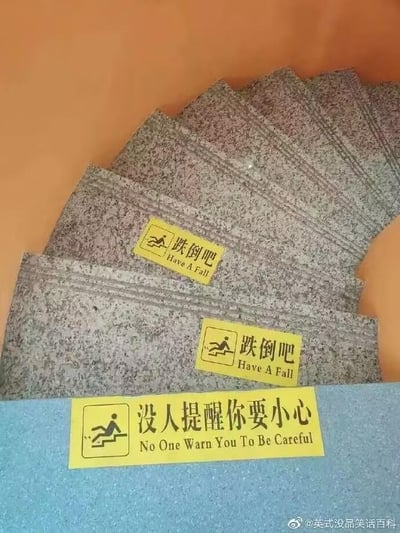 图片拍摄了楼梯区域的三组黄色警示贴，前两张贴在灰色的楼梯台阶上，印着卡通跌倒小人图案和文字“跌倒吧 Have A Fall”，最后一张贴在楼梯底部的蓝色平台上，同样配有跌倒小人图案，文字为“没人提醒你要小心 No One Warn You To Be Careful”。这组警示贴不走寻常路，用反向的、无厘头的话术来提醒人们上下楼梯注意安全，正经的提醒需求用搞笑的反讽方式表达，形成强烈的反差感，让人忍俊不禁。