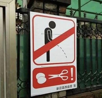 图片中展示了一块张贴在金属栅栏上的标识牌，背景可见石质立柱和绿色遮阳棚。标识牌主体为白色底红色边框，上方区域有一个黑色人形剪影正在小便的图案，被一条红色斜杠贯穿，表示禁止随地小便；下方为红色矩形区域，内有白色剪刀图标正在剪切两个圆形图案，右下角标注“新莊區西盛里 製”字样，推测为台湾新北市新庄区西盛里制作的社区公告标识。