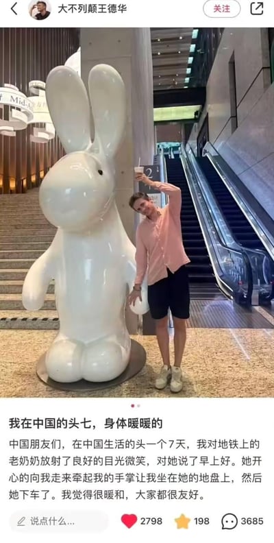这是一条外国博主发布的社交媒体动态，配图里博主和商场中的白色兔子雕塑合影，模仿雕塑的姿势，手举饮品，神态开心。动态文案玩了“头七”的谐音梗，实际指自己来到中国生活的第一个七天，分享了在地铁上的暖心经历：他向地铁上的老奶奶微笑问好，老奶奶开心地牵起他的手，让他坐在自己的座位上，之后老奶奶下车离开，博主因此感到十分温暖，感慨大家都很友好。
谐音梗说明：文案中的“头七”是趣味表述，谐音“第一个七天”，并非传统丧葬文化中的“头七”，用谐音制造轻松的表达效果。