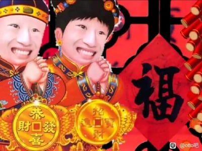 图片中两个人物穿着传统中式婚礼服饰，戴着华丽头饰，面带夸张笑容，双手合十作揖。他们手中各持一个金元宝，上面写着“恭喜发财”和“招财进宝”。背景是红色调，中央有一个大大的“福”字，右侧有鞭炮装饰，整体呈现出浓厚的春节喜庆氛围。